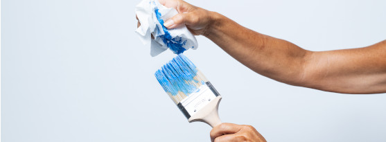 Bilden visar en hand och en målarpensel med blå färg på