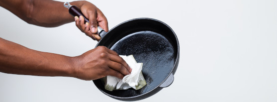 Torka ur och samla upp fett Bilden visar en hand som torkar ur en stekpanna med hushållspapper