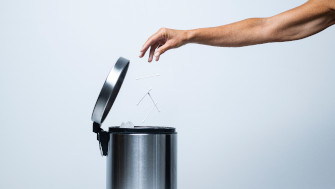 Bilden visar en hand som slänger sopor i en papperskorg