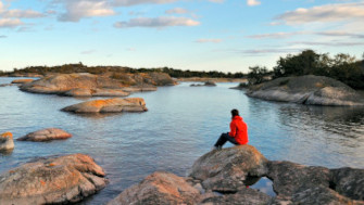 Bilden visar en person som sitter på en sten i en skärgårdsmiljö